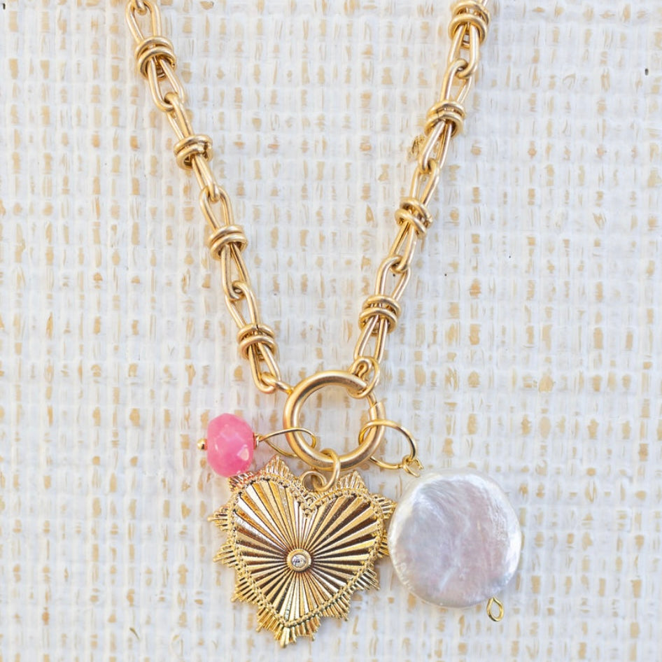Picture of gold toggle chain with a gold heart pendant with a diamond in the center, large pearl disc and small pink bead charm attached.