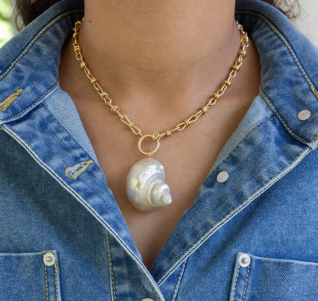 Gold chain necklace with a large pearl shell pendant worn by a person in a denim jacket.