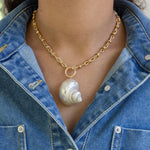 Gold chain necklace with a large pearl shell pendant worn by a person in a denim jacket.