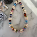 Necklace with large thin wooden disc beads and multicolored beads on a marble surface
