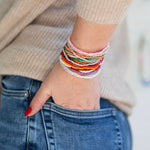 Person wearing multiple colorful bracelets on a blurred background
