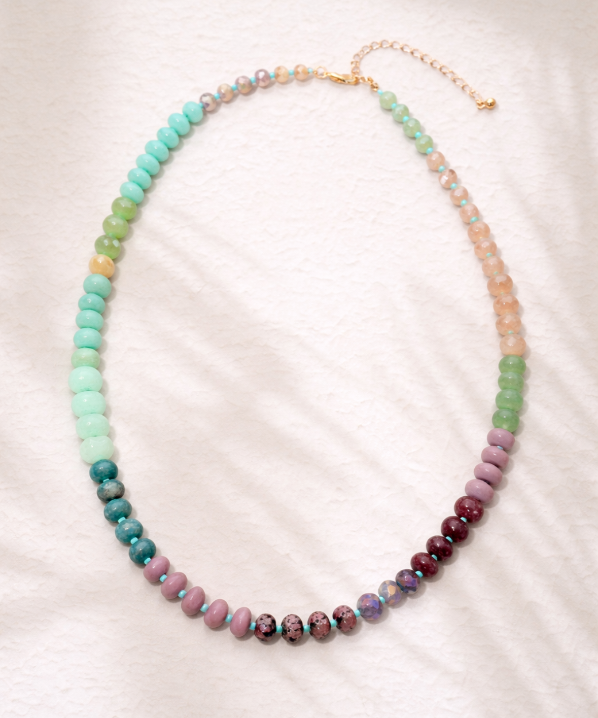 Multicolored green, coral and pink beaded necklace on a white background