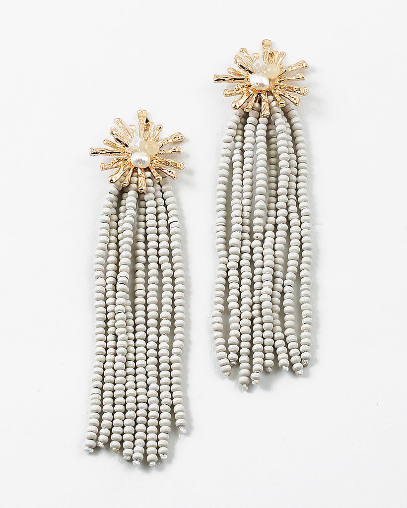 Gold starburst earrings with a pearl center and 8 white bead strands dangling from them.