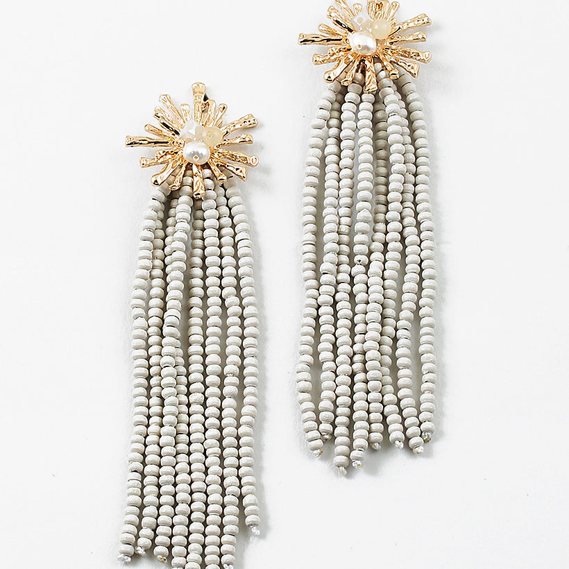 Gold starburst earrings with a pearl center and 8 white bead strands dangling from them.