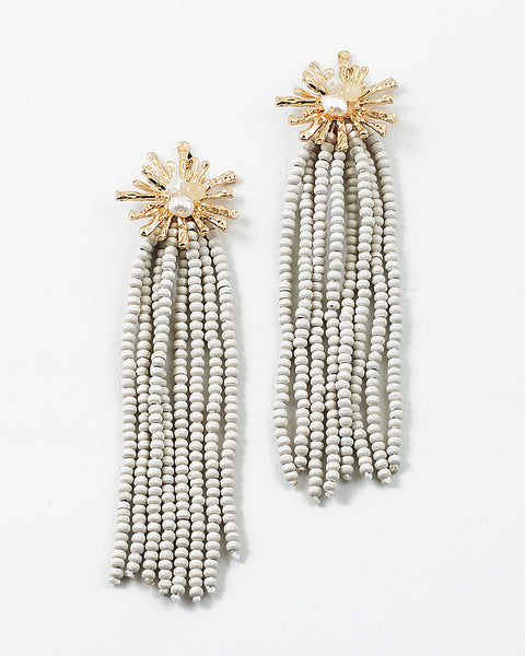 Gold starburst earrings with a pearl center and 8 white bead strands dangling from them.