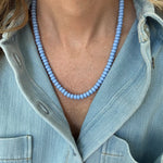 Person wearing a light blue beaded necklace with a denim jacket.