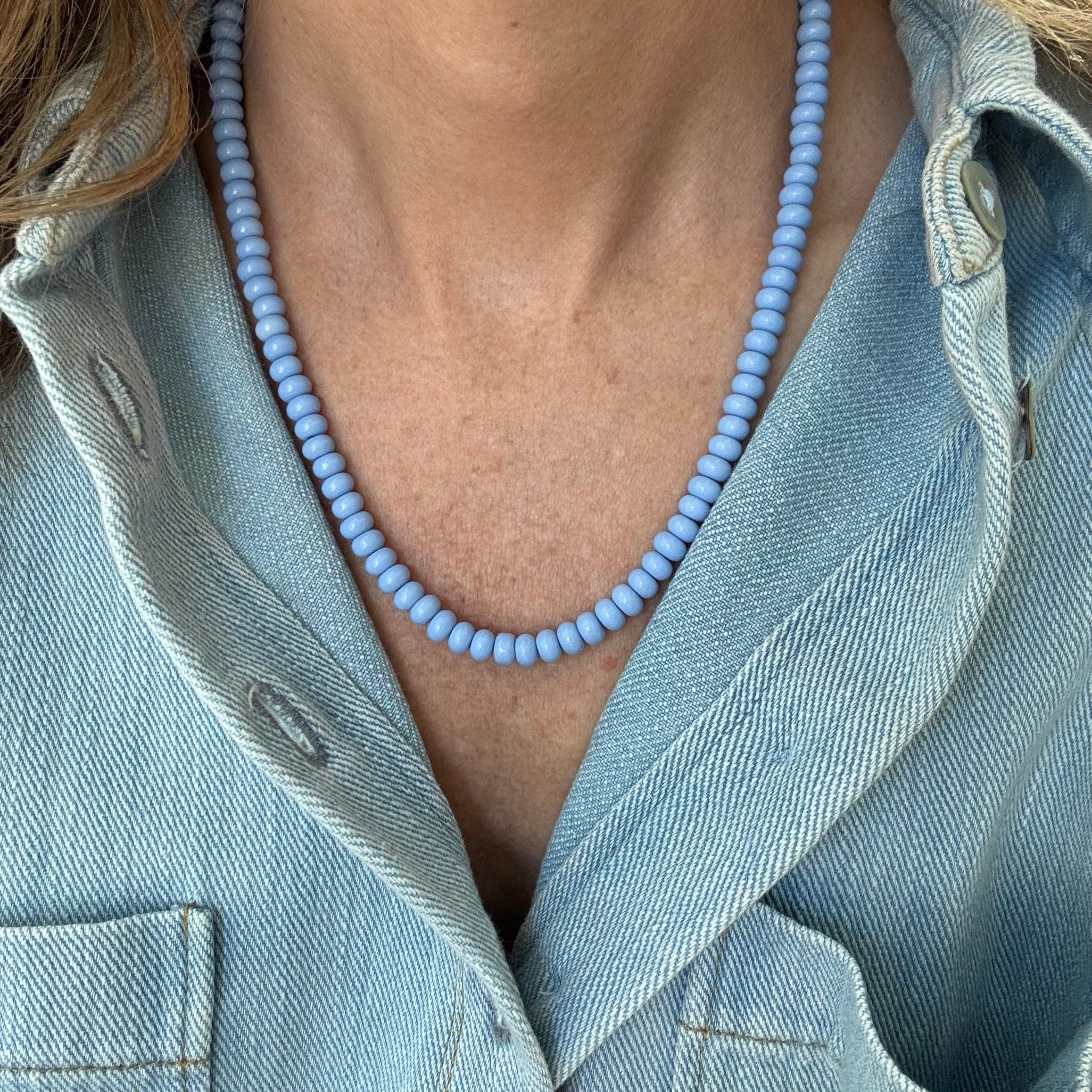 Person wearing a light blue beaded necklace with a denim jacket.