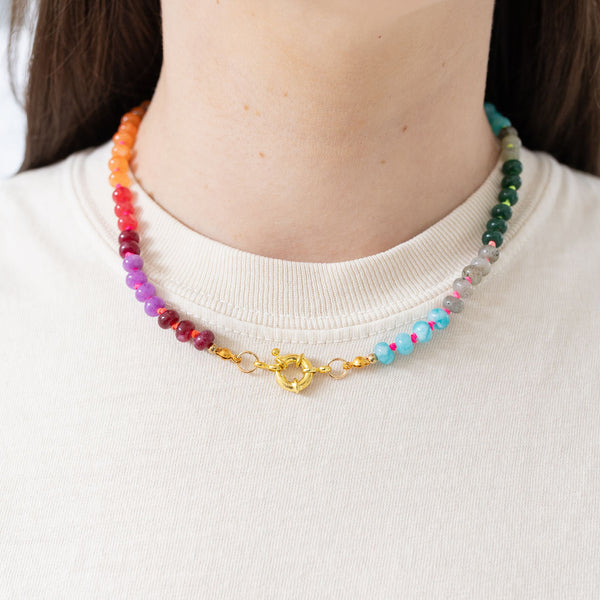 Model wearing a multi-colored beaded necklace of maroon, purple, orange, green and light blue.