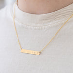 Model wearing fine gold chain necklace with a gold bar pendant that reads, "Love".