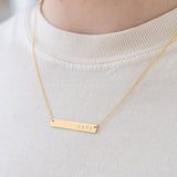 Model wearing fine gold chain necklace with a gold bar pendant that reads, "Love".