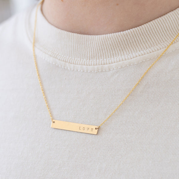 Model wearing fine gold chain necklace with a gold bar pendant that reads, "Love".