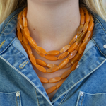 6 layered orange bead necklace worn by a person with a denim jacket