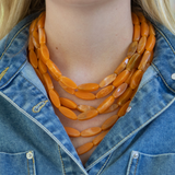 6 layered orange bead necklace worn by a person with a denim jacket