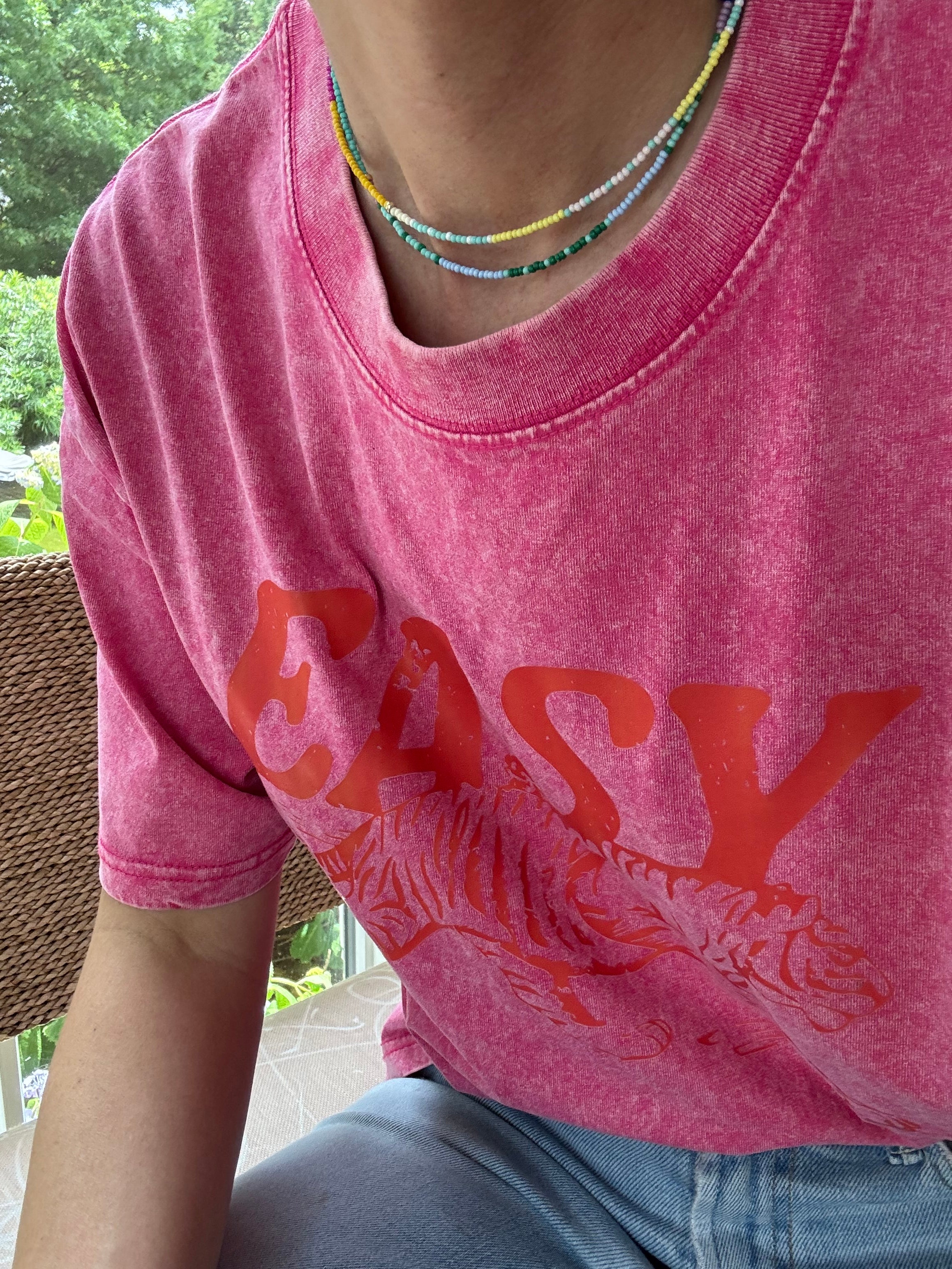 Picture of a woman wearing a pink Tshirt and two dainty bead necklaces. One necklace is yellow and white, one in dark and light blues.