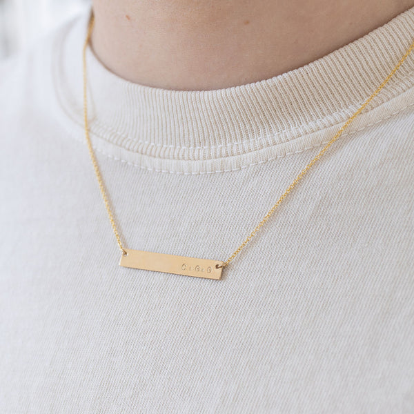 Picture of model wearing a fine gold chain with a gold bar pendant.