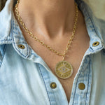 Woman wearing a necklace around her neck with a gold link chain with a circle medallion and an eye in the middle