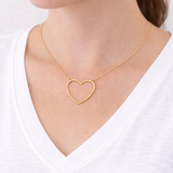 Gold heart-shaped necklace worn by a person on a white background