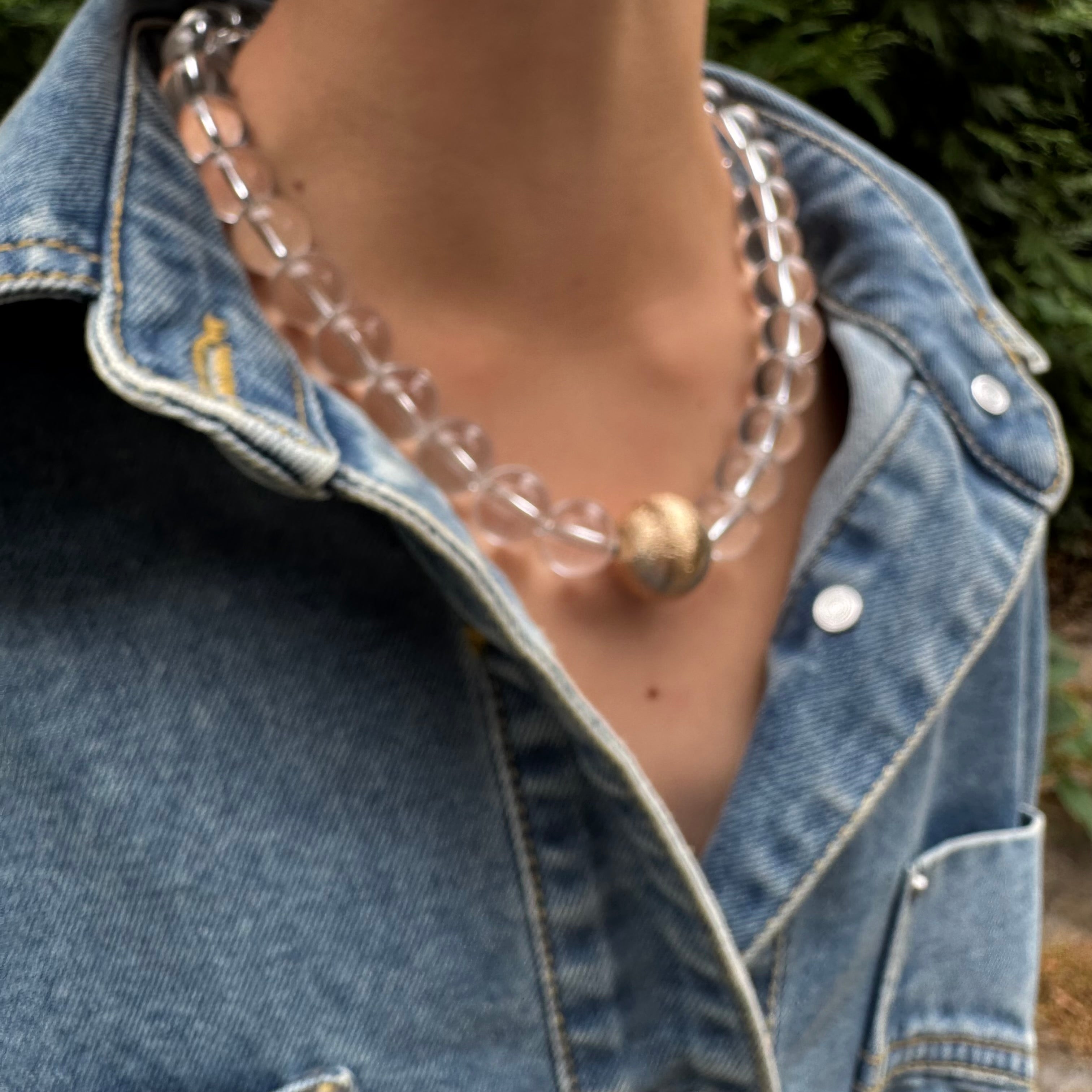 Person wearing a clear beaded necklace with a denim jacket
