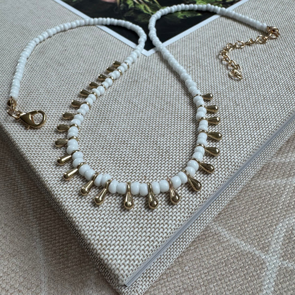 Picture of a white bead necklace with gold teardrop beads alternating through its center.