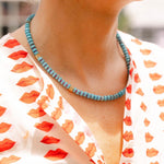 Woman outside wearing a white dress with a red lips print and a blue/gold beaded necklace around her neck