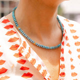 Woman outside wearing a white dress with a red lips print and a blue/gold beaded necklace around her neck