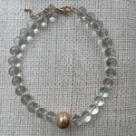 Chunky clear bead necklace with large gold bead at its center.