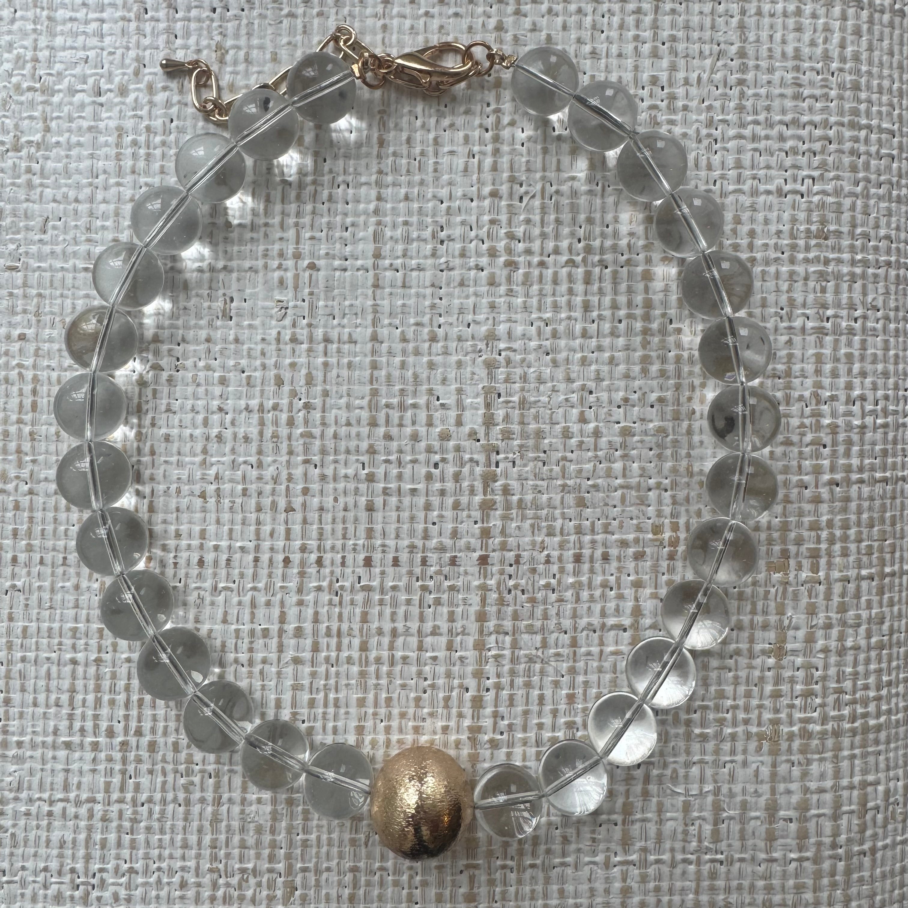 Chunky clear bead necklace with large gold bead at its center.