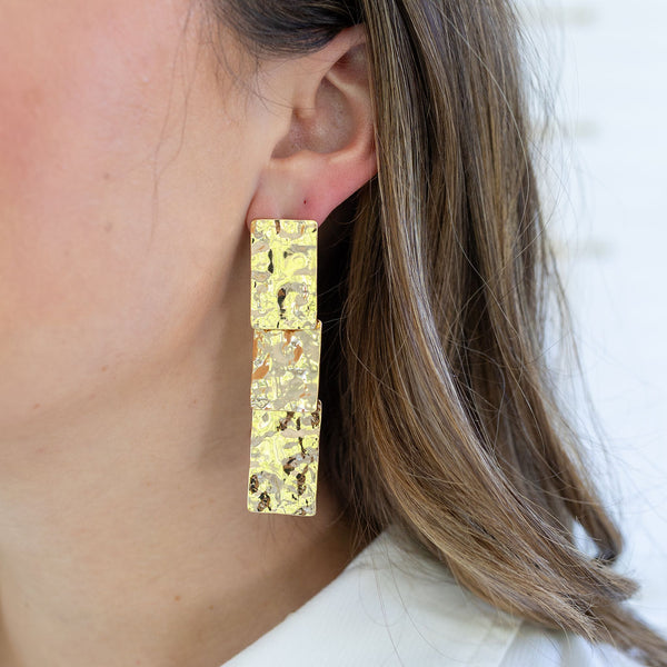 Woman wearing a hammered gold dangle earrings of three stacked rectangles.