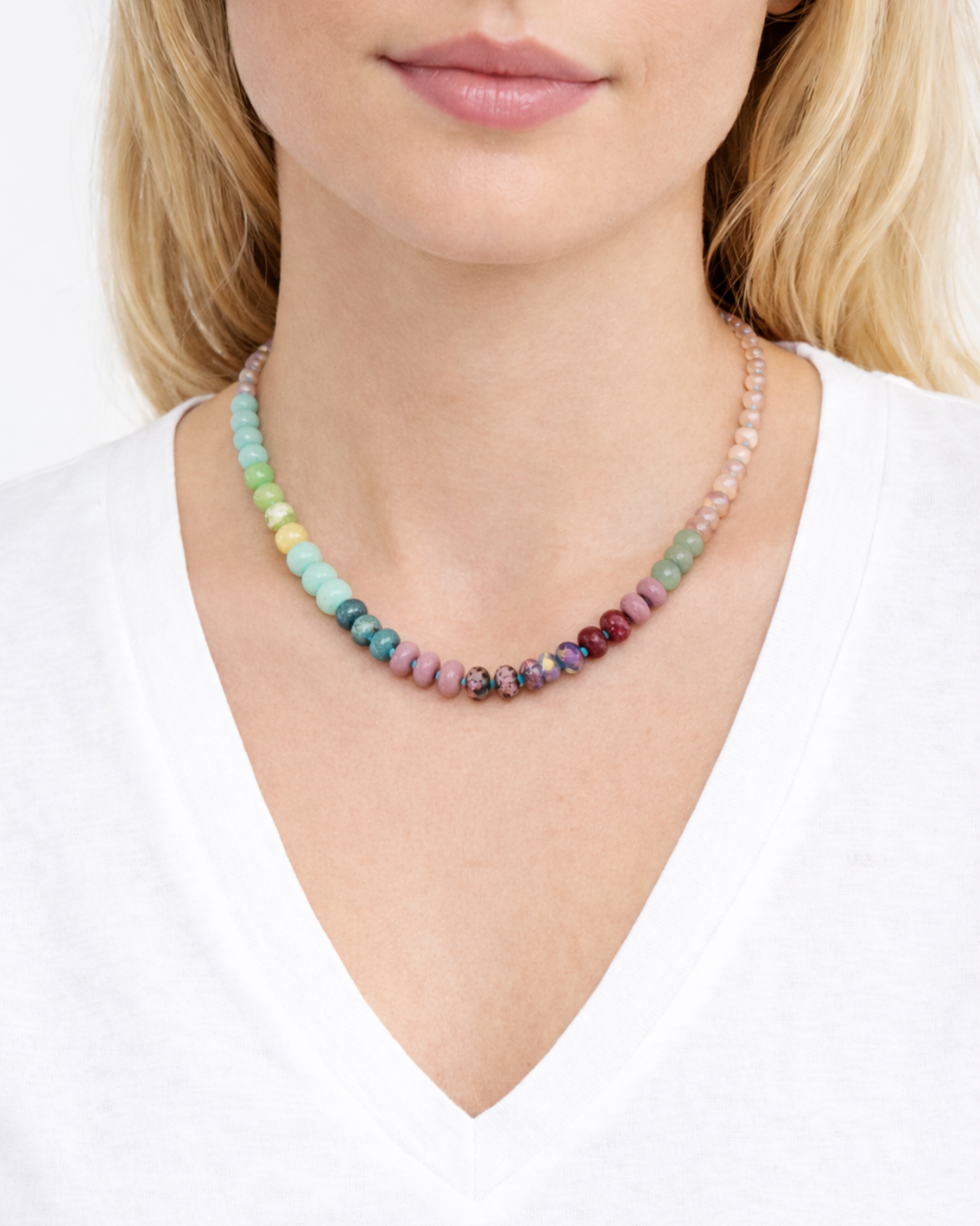 Multicolored green, pink and coral beaded necklace worn by a person on a white background