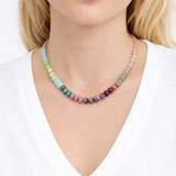 Multicolored green, pink and coral beaded necklace worn by a person on a white background