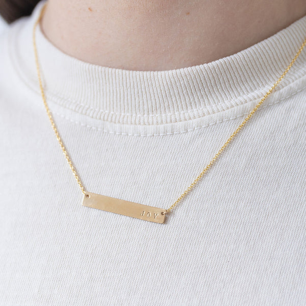 Picture of fine gold chain with a gold bar pendant that reads, "Joy".