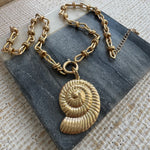 Picture of a gold link chain necklace with a gold toggle clasp and a large gold seashell charm at its center.