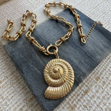 Picture of a gold link chain necklace with a gold toggle clasp and a large gold seashell charm at its center.