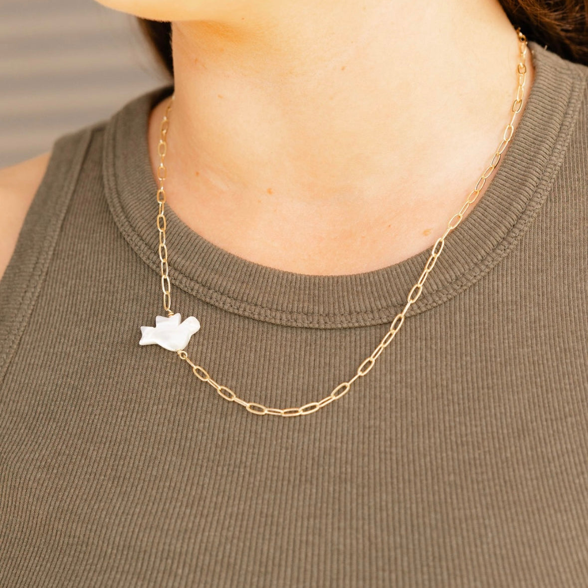 Gold chain necklace with a small pendant worn by a person in a green sleeveless top.