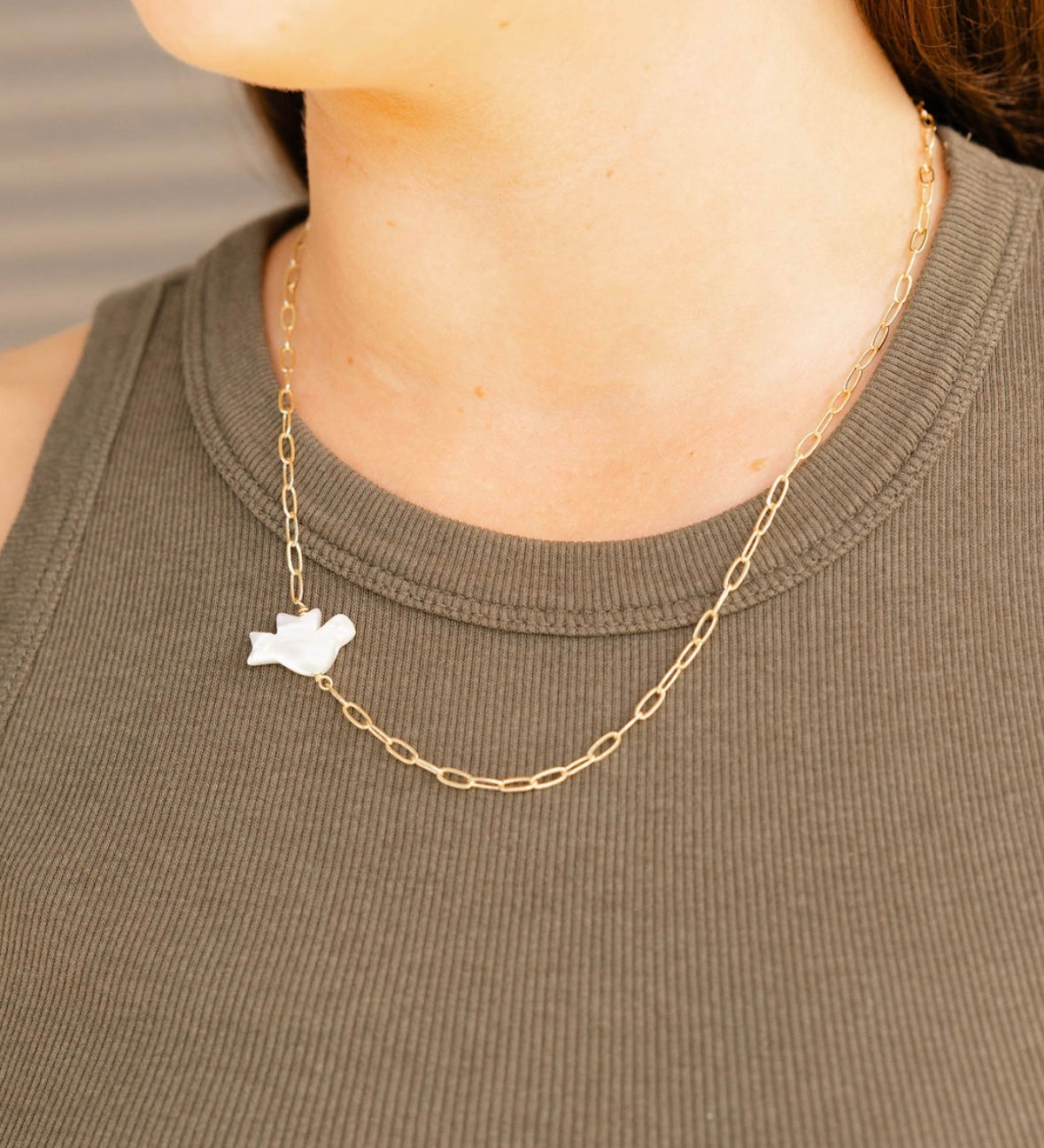 Gold chain necklace with a small pendant worn by a person in a green sleeveless top.