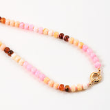Necklace with multicolored pink and peach beads and a gold clasp on a white background