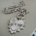 Close up of a large link silver chain with a toggle clasp and a large textured heart pendant.