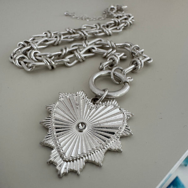 Close up of a large link silver chain with a toggle clasp and a large textured heart pendant.