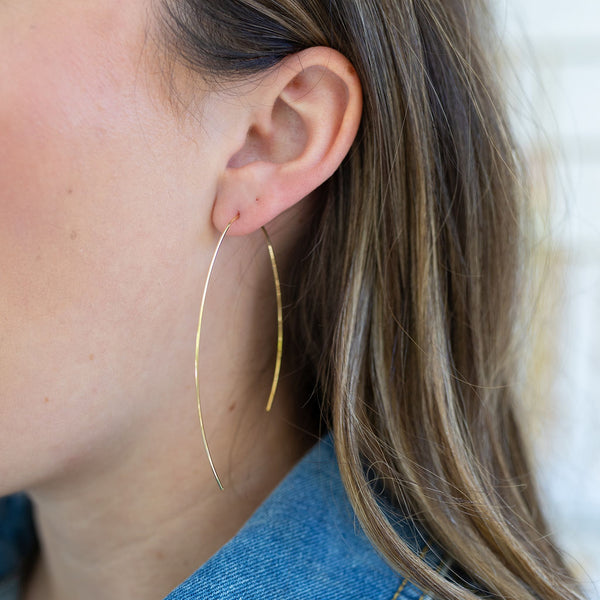 Picture of a woman's ear with a gold wire strand threaded through as an earring.