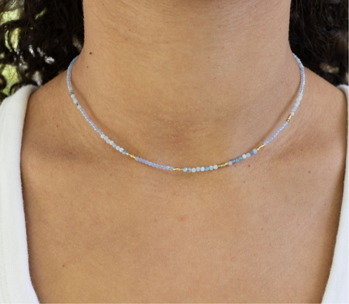 Picture of a woman wearing a delicate bead necklace in tiny white, gold and blue beads.