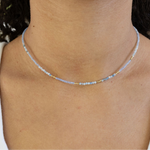 Picture of a woman wearing a delicate bead necklace in tiny white, gold and blue beads.