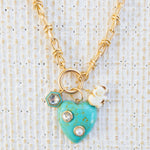 Picture of gold toggle chain with a large turquoise heart with diamond and pearl inlays. Necklace has a white elephant charm and a diamond with turquoise border charm.