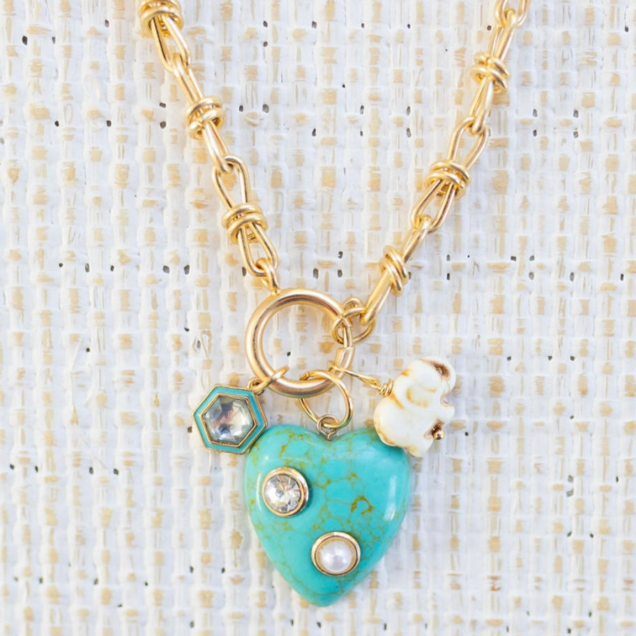Picture of gold toggle chain with a large turquoise heart with diamond and pearl inlays. Necklace has a white elephant charm and a diamond with turquoise border charm.