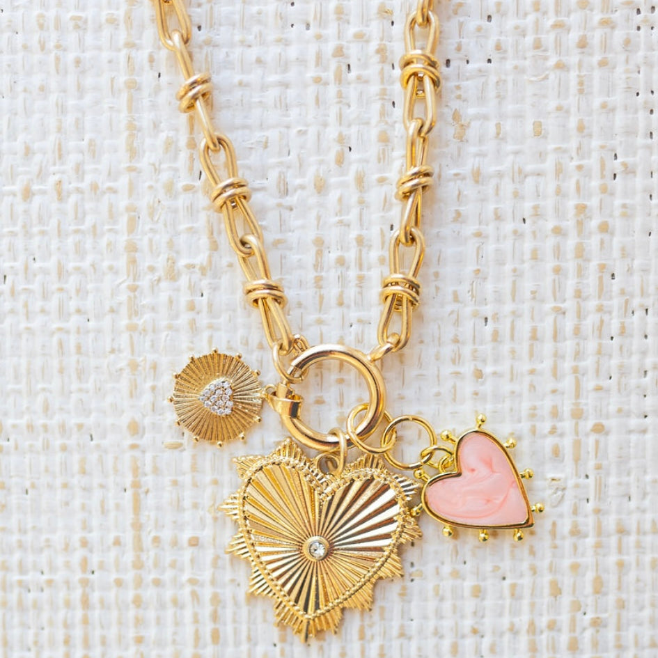 Picture of gold toggle chain with a pink heart charm, a textured gold charm with diamond heart and a large gold heart pendant with a diamond in the center.