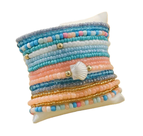 Picture of a small pillow displaying 16 different bracelets in Beach themed colors.  Bracelets are shades o white, corals, pinks, blues and amber.
