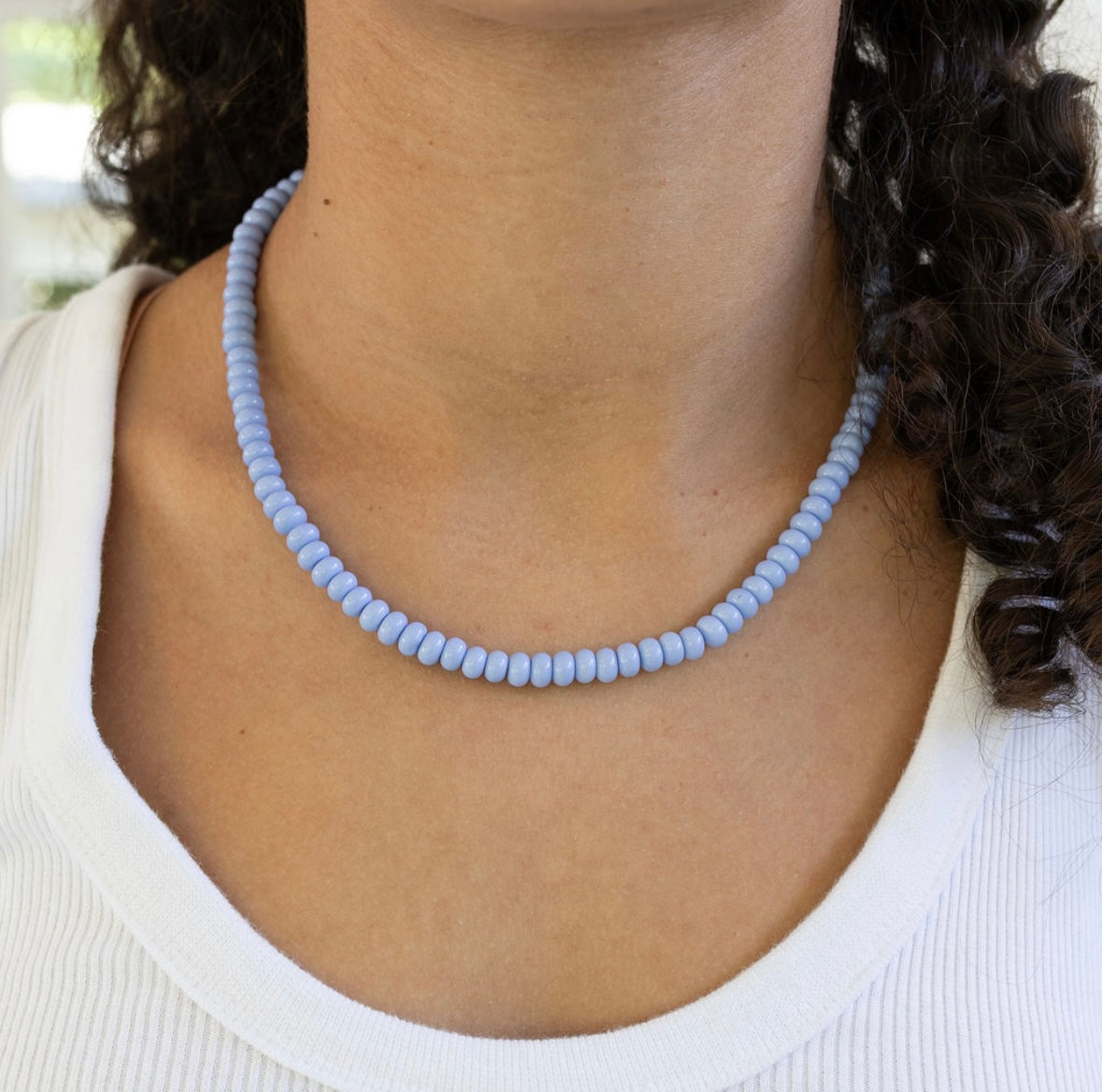 Person wearing a light blue beaded necklace with a blurred background