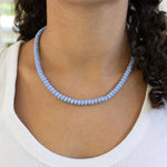 Person wearing a light blue beaded necklace with a blurred background
