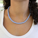 Person wearing a light blue beaded necklace with a blurred background
