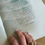 Handwritten text on a piece of paper with a hand holding it, wearing a gold ring.