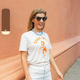 Woman wearing sunglasses and a cream shirt with an orange print of a cowgirl with a lasso and the text "Stay Wild" with multiple blue beaded necklaces